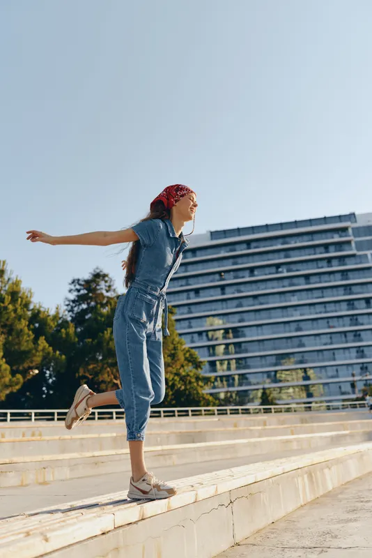 Lifestyle woman in modern boho-western denim street style balancing outdoors in bright sunlight, vibrant film color capturing free-spirited urban energy and fashion.