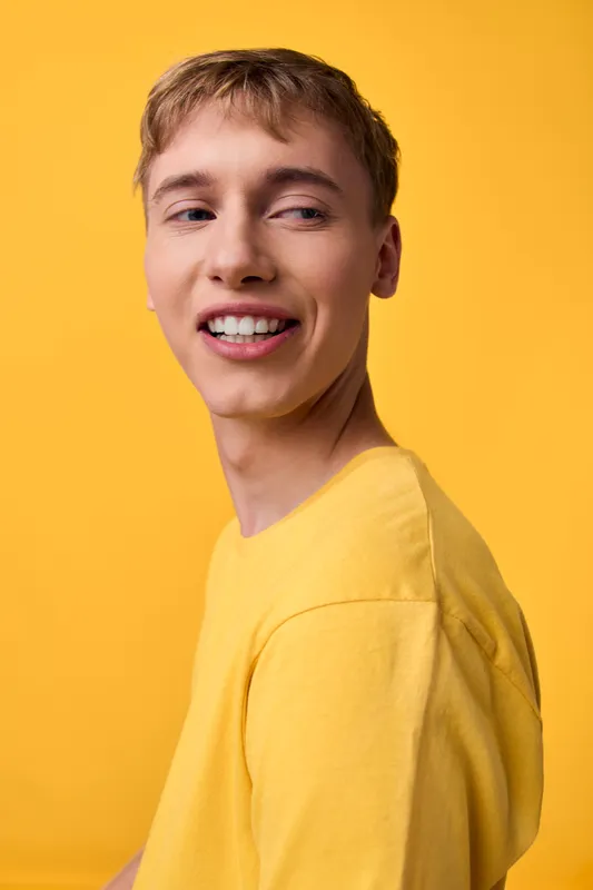 Smile, young man in a yellow shirt against a bright yellow backdrop, conveying upbeat mood, casual style, and friendly energy for lifestyle, fashion, and advertising visuals