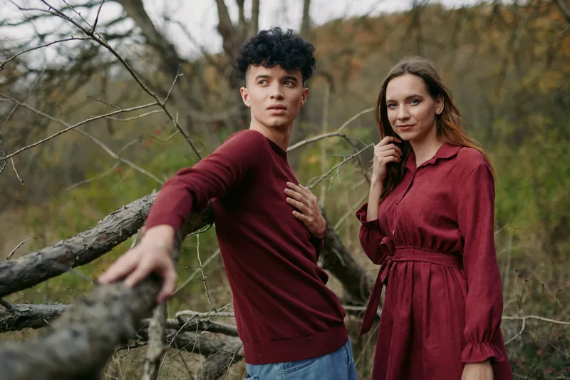 Young couple posing outdoors in a natural autumn landscape, relaxed and connected with genuine expressions that convey authenticity and quiet credibility in an intimate portrait style.