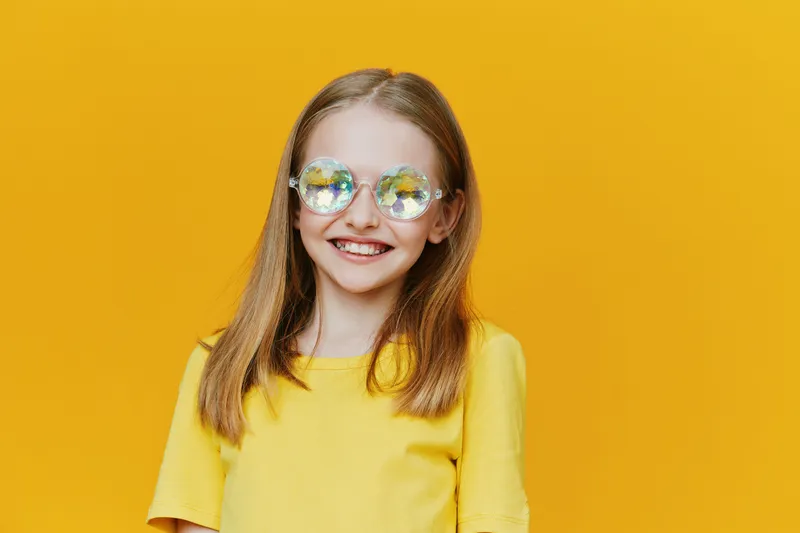Joyful young girl with stylish glasses wearing a bright yellow shirt against a vibrant yellow background, embodying summer vibes and cheerful energy
