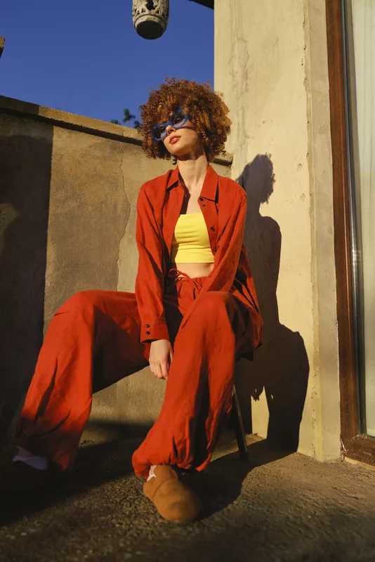 Woman lifestyle fashion urban rooftop outdoor sunlight casual bold color orange yellow suit clothing style pose confidence sunglasses curly hair portrait mood warm energy