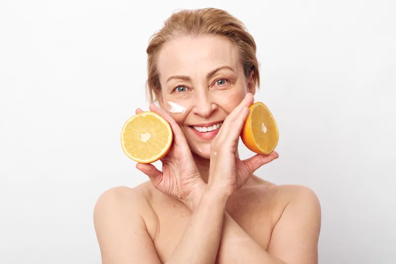 Smiling mature woman with natural skin holds two halves of fresh citrus fruit near face. Concept of healthy lifestyle, skincare, natural beauty, wellness, and organic self-care with vitamin boost.