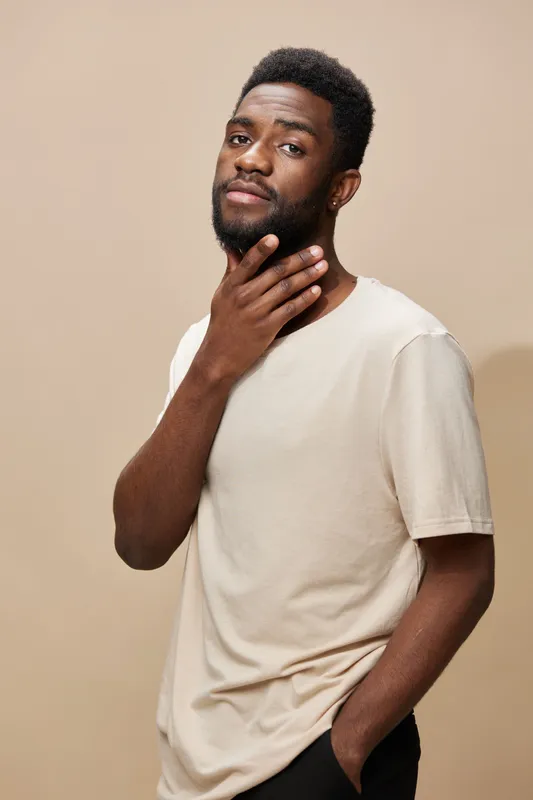 Confident male model poses thoughtfully against a light beige background, wearing a casual beige t shirt, exuding a sense of self assurance and contemplation