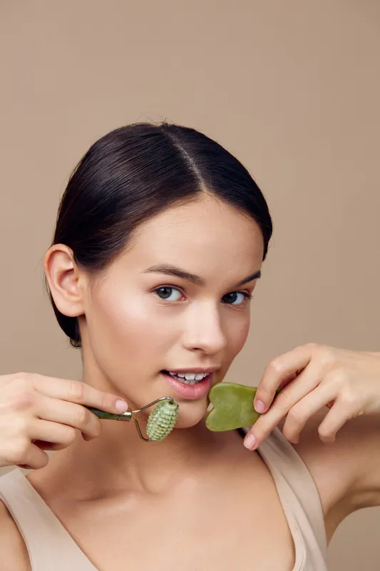 Young woman practicing skincare with jade roller and gua sha tool, showcasing healthy skin and beauty routine in a serene setting