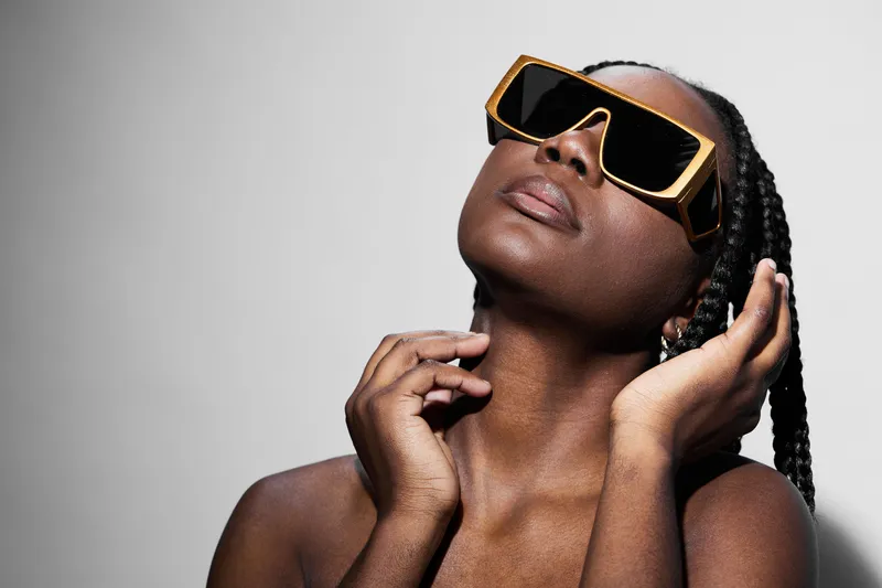 Stunning portrait of a woman with braids wearing bold sunglasses, showcasing confidence and elegance against a minimalistic background