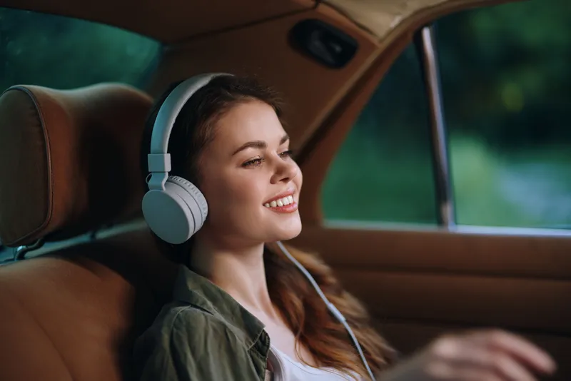 Young woman enjoying music in a car with headphones, relaxed expression, cozy interior, natural light, perfect for lifestyle and travel concepts.