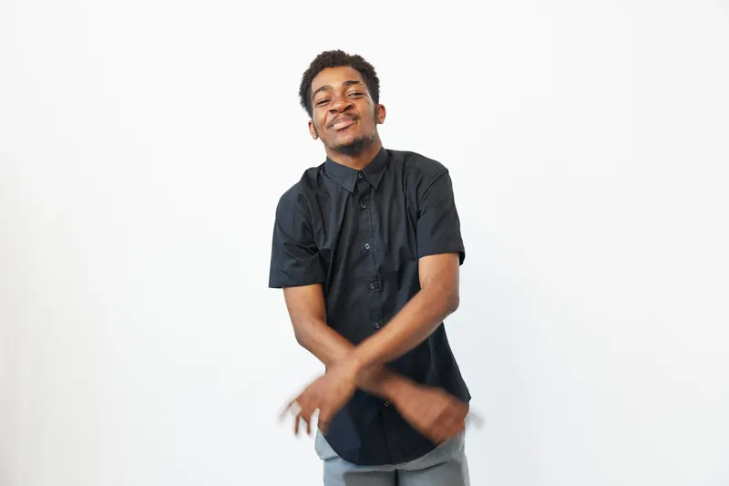 A cheerful black man wearing a casual shirt, smiling and posing against a plain white background, representing joy and confidence in every day.