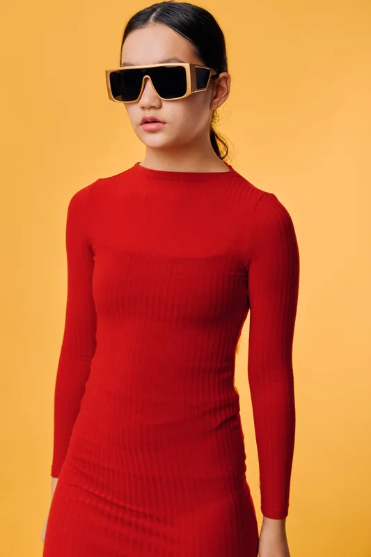 Woman in red dress wearing oversized sunglasses posing on orange background with serious expression and sleek hairstyle for fashion or style concept portrait.