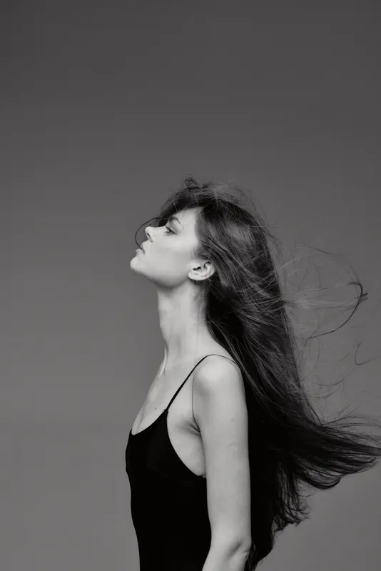 Black and white profile of a young woman with long hair in a sleeveless top, expressing calmness and grace with flowing hair against plain background.