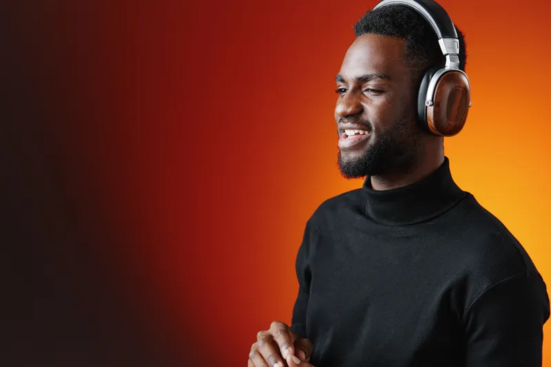 Happy African man enjoying music with headphones, modern casual attire, warm gradient background, uplifting emotions, perfect for music and lifestyle themes