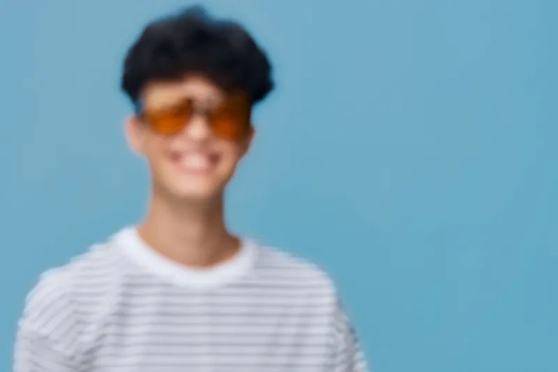 smiling man wearing striped shirt and orange sunglasses with curly hair, happy expression on blue background, casual style portrait