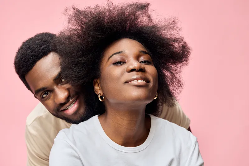 A joyful African couple with natural hair, expressing love and happiness against a soft pink background, representing warmth, affection, and connection in contemporary lifestyle photography