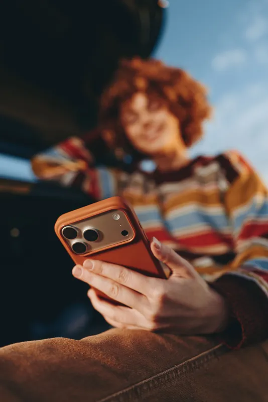 Woman holding smartphone, lifestyle moment outdoors, curly hair soft focus, she smiles while texting, communication and social media, casual sweater, warm natural light, technology privacy