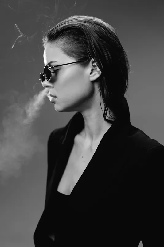 Black and white portrait of a young woman wearing sunglasses with smoke silhouette, stylish and mysterious mood.