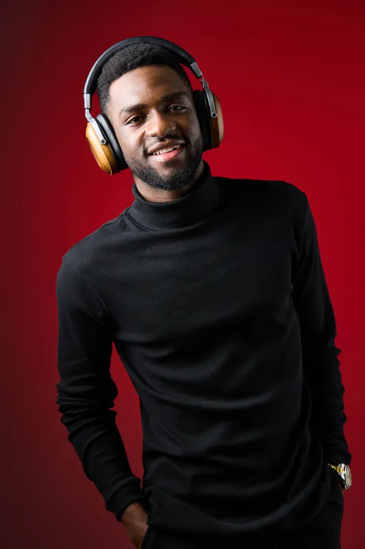 Young man wearing headphones, smiling with a confident expression against a vibrant red background, showcasing a modern lifestyle and music appreciation