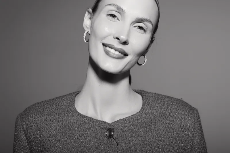 Portrait of a smiling caucasian woman with light skin wearing earrings and a textured top on grey background. Concept of happiness and fashion.