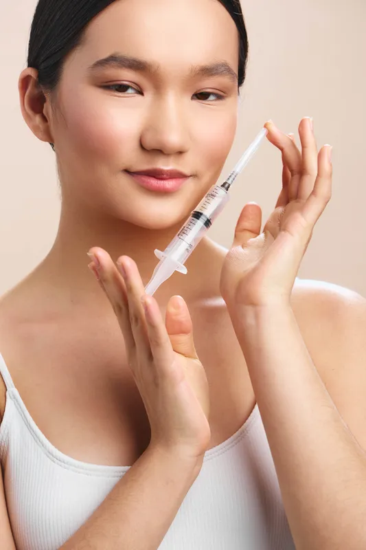 asian woman is shown preparing a syringe in a clinical setting, displaying calm concentration and careful technique, with soft lighting creating a professional medical atmosphere.