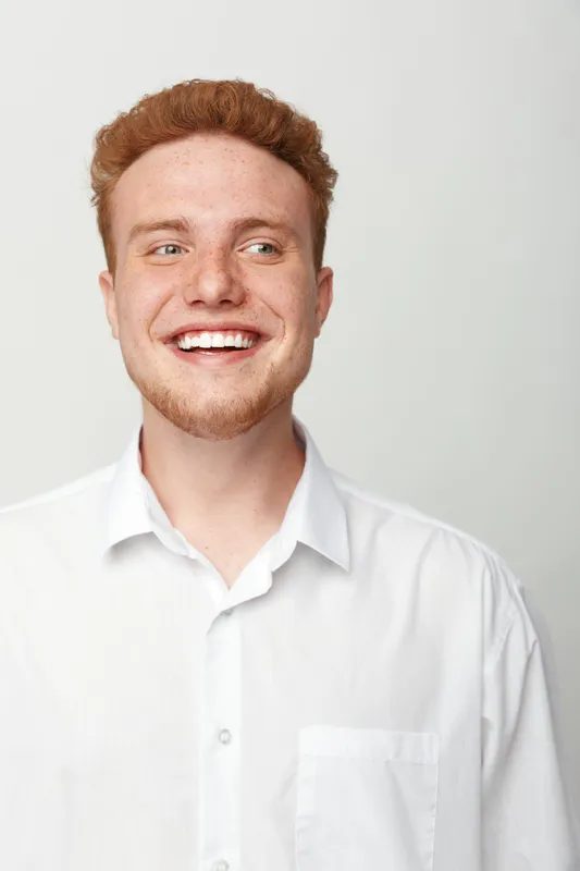 Smiling young man with red hair and beard wearing white shirt looks away with happy expression. Studio portrait on light background. Concept of youth, confidence, and positive mood.