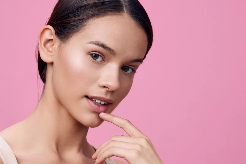 Young woman with natural beauty and soft smile on pink background, showcasing skincare and healthy lifestyle concepts