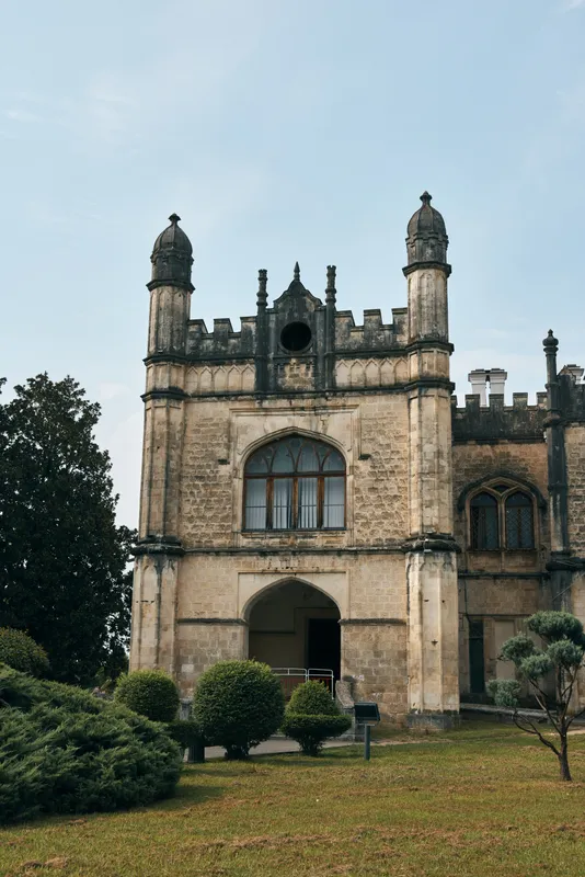 Castle facade rises over a manicured garden, featuring arched doorway, turrets, and weathered stonework, capturing historic architecture and a timeless estate atmosphere in tranquil grounds