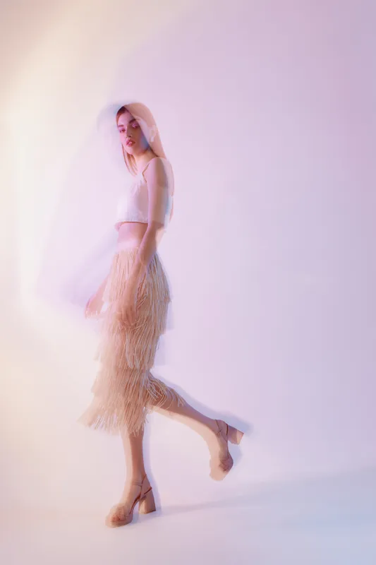 Woman beauty fashion model in a fringed skirt and sleeveless top walking with soft motion blur on a light background. Concept of style elegance and modern trends.