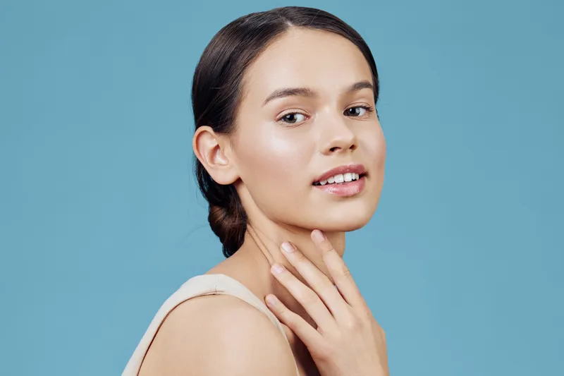 Portrait of a young woman with long brown hair, natural makeup, and a gentle smile against a solid blue background, expressing confidence and beauty