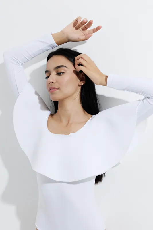 Woman sport fitness wearing stylish white athletic outfit with a unique modern design posing gracefully against a plain white background in natural light.