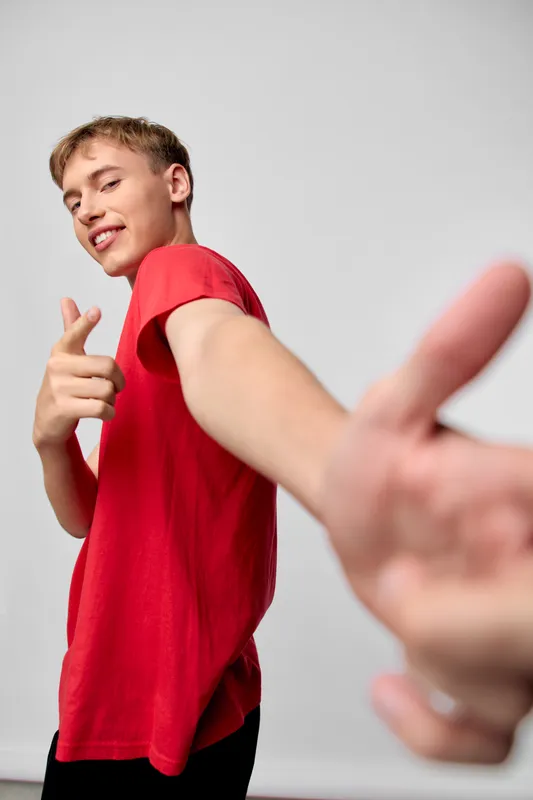 Dynamic shot of a man in a red shirt reaching forward with a confident smile, creating energy and movement in a clean studio, ideal for lifestyle, fashion, or promotional campaigns.