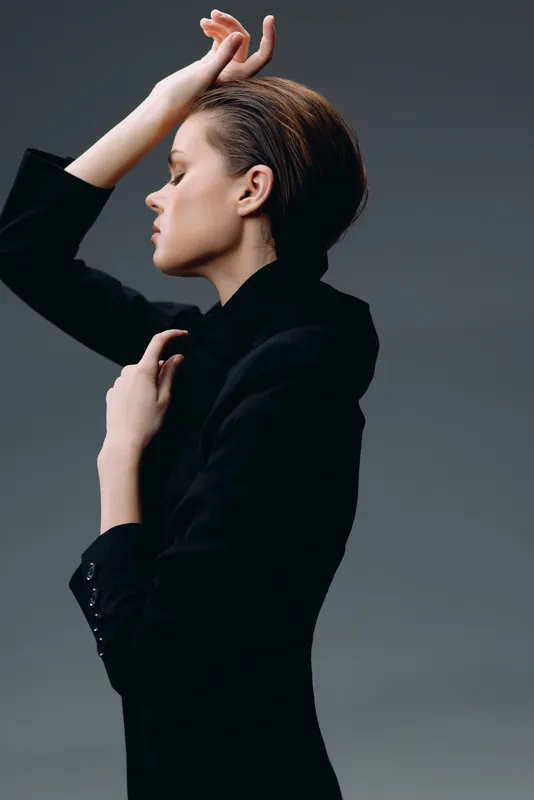 Elegant woman in black outfit posing gracefully with eyes closed, showcasing stylish fashion and calm expression.