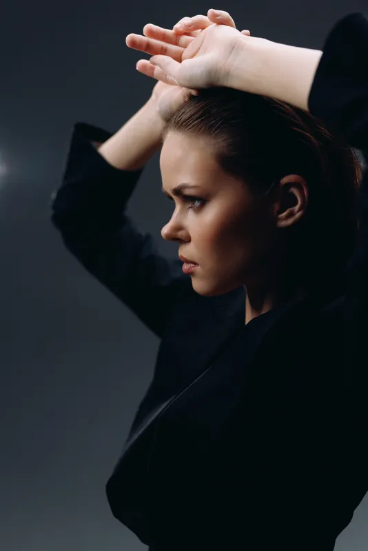 Profile of a serious woman in black clothing with hands raised, showing determination and focus in low light.