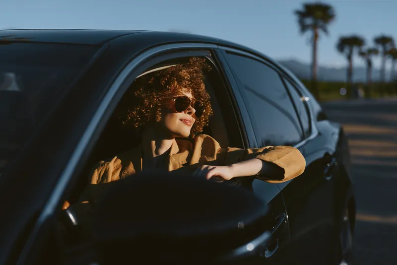 A woman lifestyle shot shows a stylish woman in a sleek car, retro film color tones, sunglasses on, enjoying the horizon, a casual moment of freedom and quiet drive.