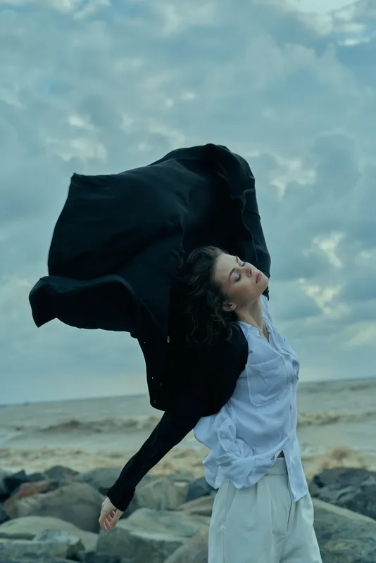 Fashion movement on the wind swept coast, a woman in a white shirt with a billowing coat, dynamic pose, outdoor style and freedom by the beach and sea