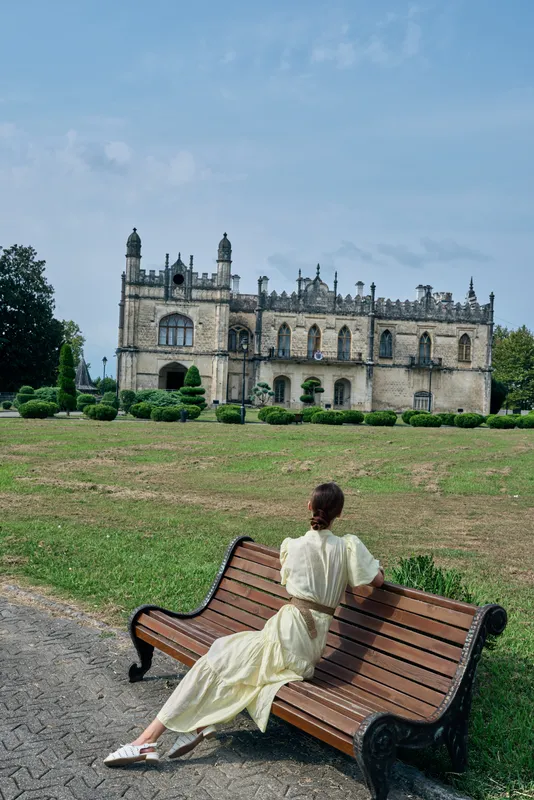 woman on bench in park viewing historic mansion architecture, vintage dress and solitude with authenticity inclusivity in travel