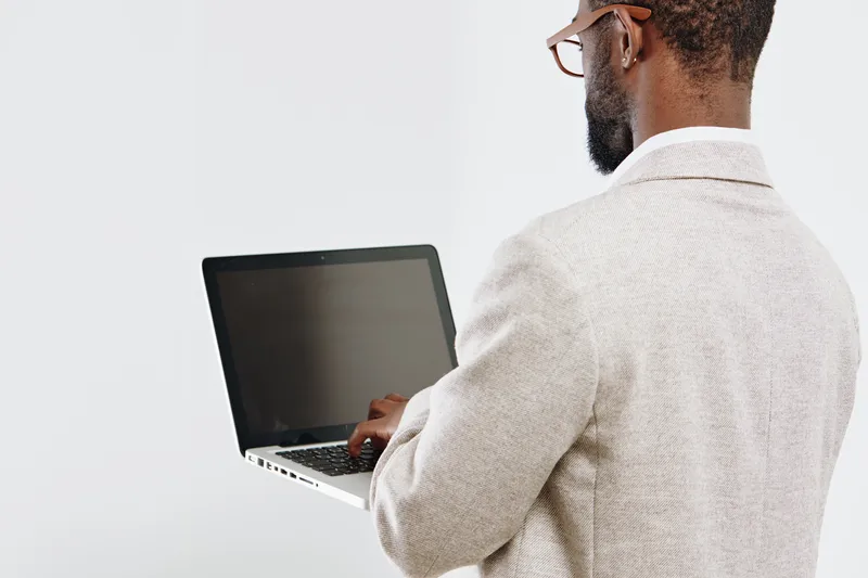 Professional man with glasses in beige blazer working on a laptop isolated on plain white background, close-up of back view. Modern technology, workplace, business concept, serious mood, office enviro