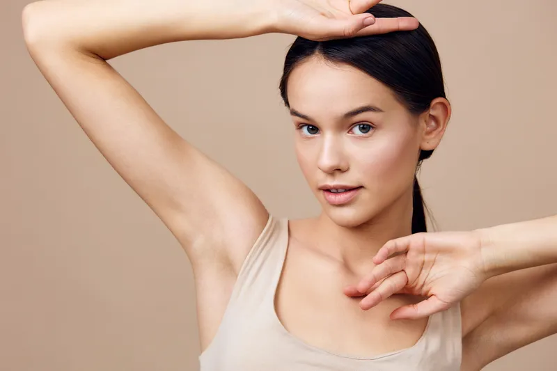 Elegant young woman posing with graceful hand gestures, showcasing natural beauty and confidence in a neutral toned background, perfect for skincare or beauty concepts