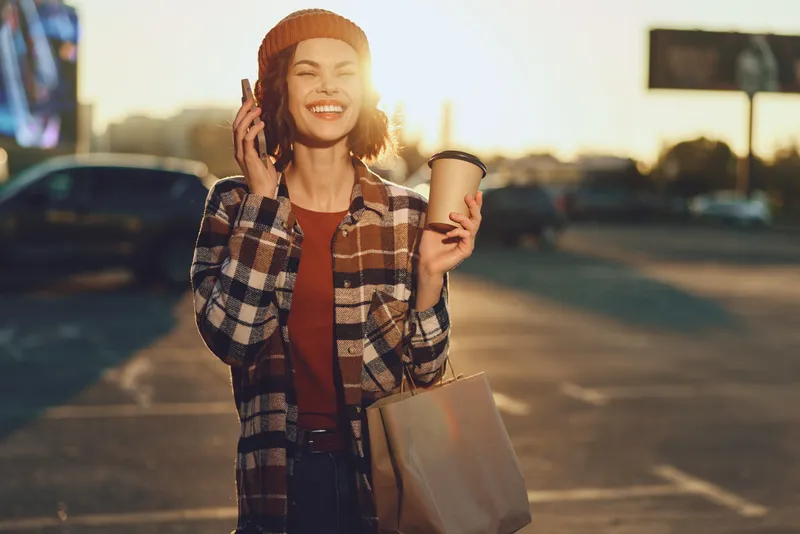 woman holding coffee and phone, smile and candid expression in golden hour glow. Urban morning portrait conveying authenticity, mindful lifestyle and emotional storytelling in city streets.