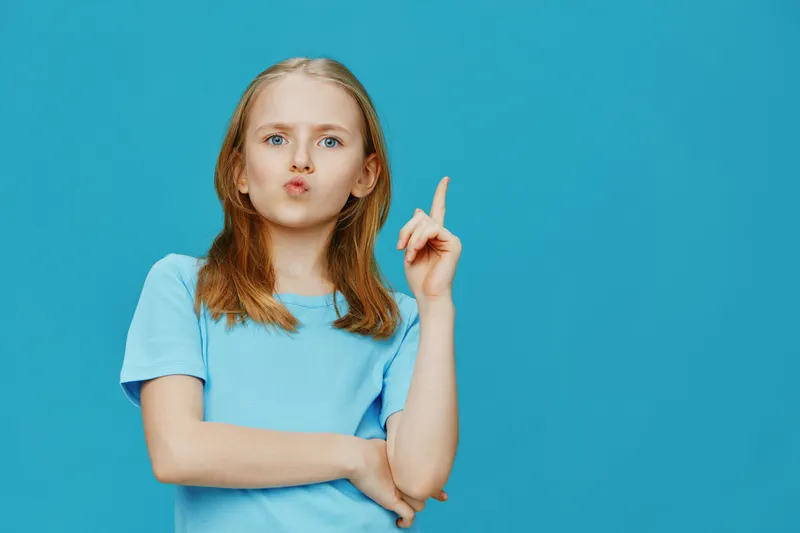 Young girl in a blue t shirt making a thoughtful expression against a bright blue background, symbolizing creativity and imagination, suitable for various concepts