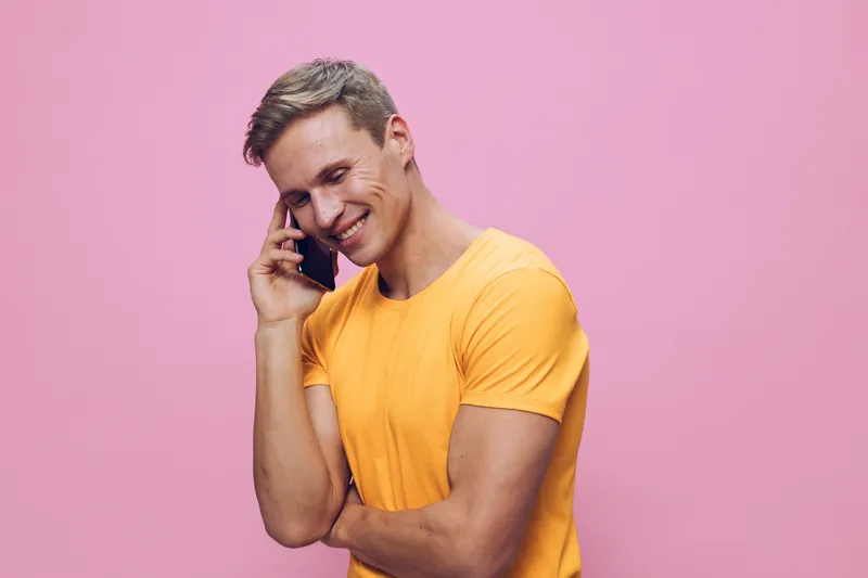Smiling young man wearing yellow t-shirt talking on mobile phone isolated on pink background, casual fashion, cheerful mood, lifestyle concept, studio portrait, bright colors, happiness, communication