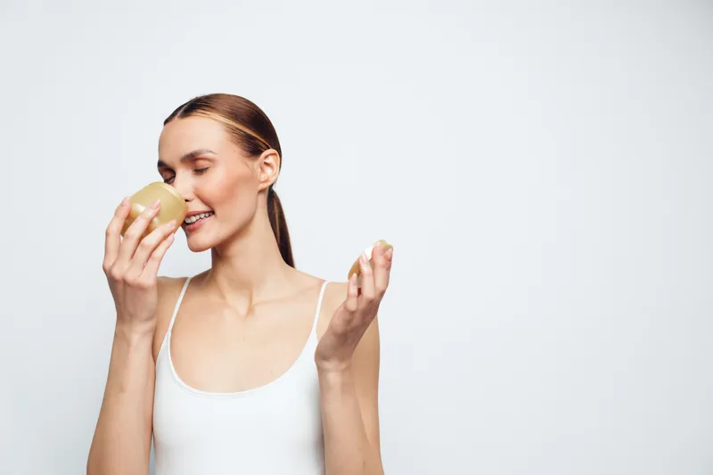 Smiling woman applying face cream with cotton pad, close up on gray studio background, skincare and self care, soft studio lighting, wellness beauty routine