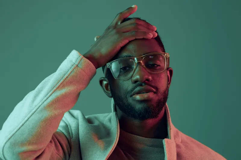 Handsome young man in stylish glasses against a green and pink background, conveying confidence and modern aesthetics with a trendy outfit