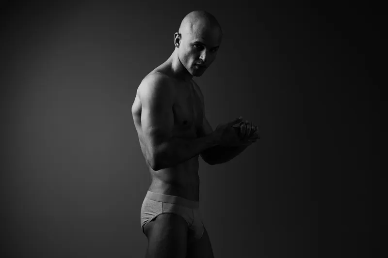 Black and white image of a muscular man posing confidently, showcasing strength and determination with an artistic lighting effect.