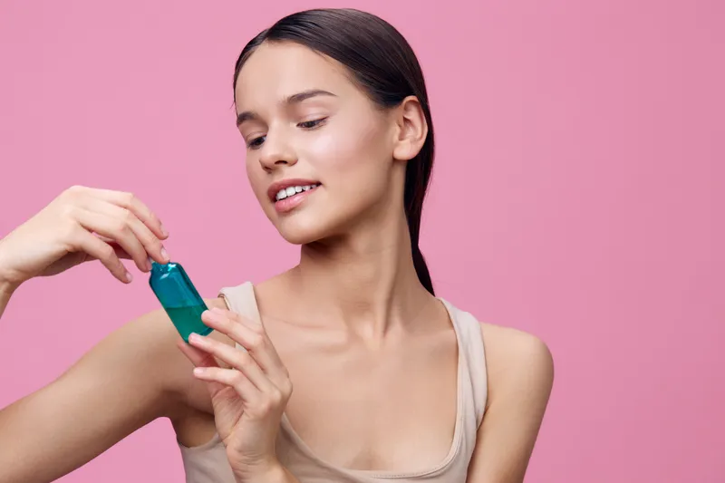 Young woman with long hair holding skincare product against a pink background, showcasing a natural beauty routine and healthy skin care lifestyle