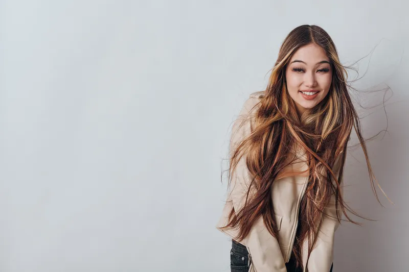 Young woman with long hair smiling and wearing casual jacket on light background. Portrait, happiness, fashion and beauty concept with natural expression and relaxed pose.