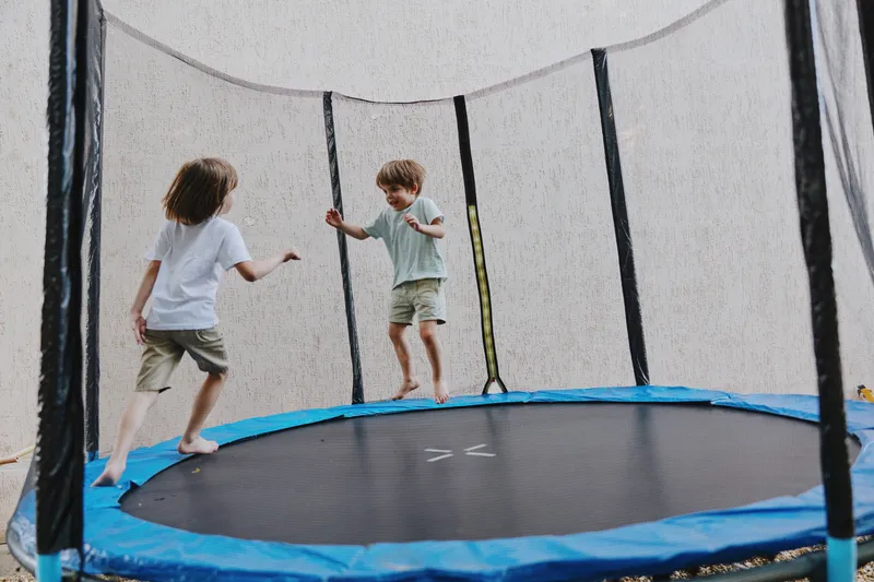 Jumping children on a trampoline, enjoying a fun outdoor activity with playful expressions and sunny vibes. A perfect moment of childhood joy captured in action.