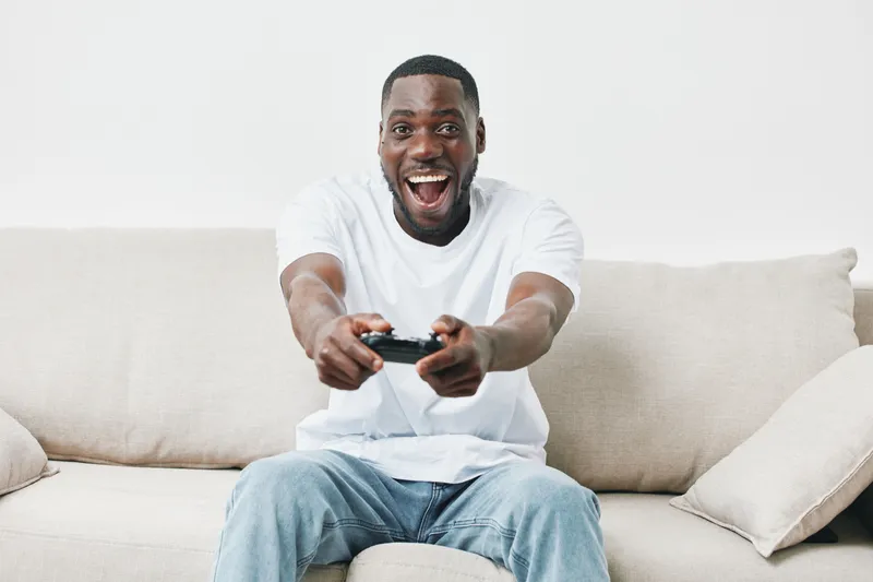 Happy young African American man playing video games on a couch, smiling and enjoying a leisure activity at home
