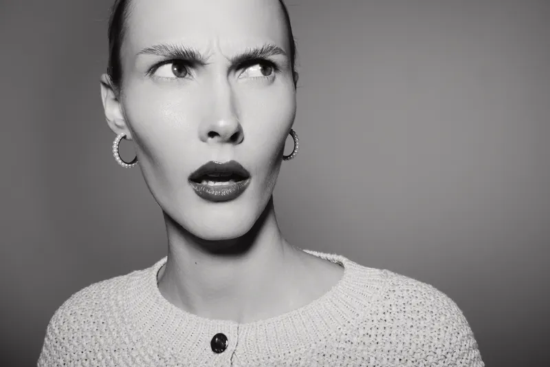 Portrait of a young Caucasian woman with pale skin and short hair looking confused and skeptical. Studio lighting highlights her facial expression and knitted sweater. Concept of doubt and