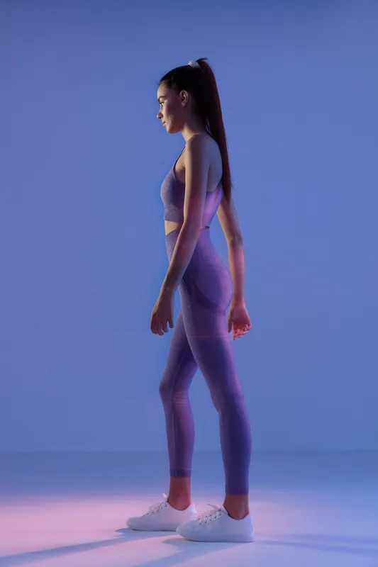 woman sport fitness wearing purple activewear in side profile pose on gradient blue background, fit healthy lifestyle, gym workout concept