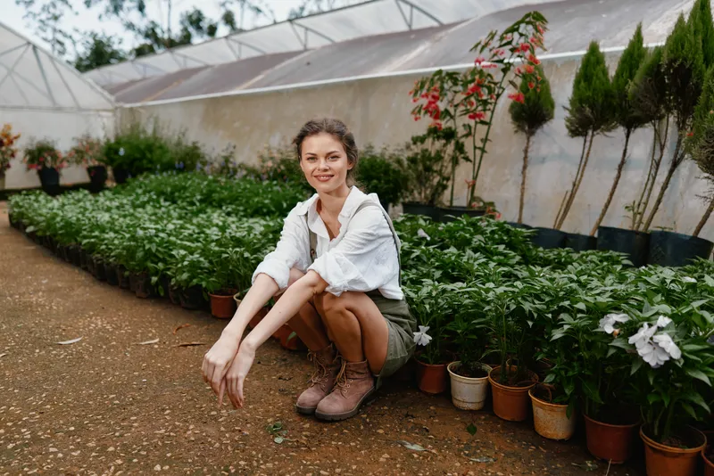 Young woman in a greenhouse, wearing casual attire, surrounded by blooming plants, showcasing a love for gardening and nature, conveying a sense of tranquility and connection with nature