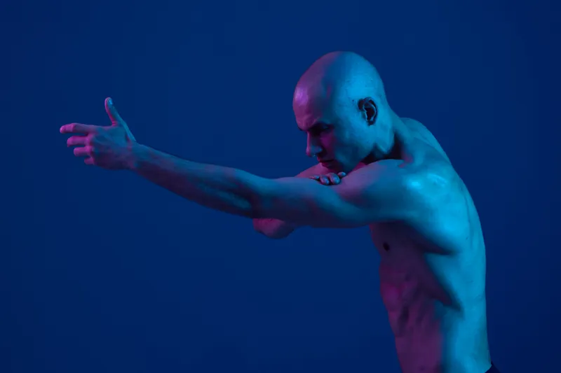 A man striking a dynamic pose with blue lighting creates an energetic and captivating atmosphere, showcasing strength and movement in monochrome tones.