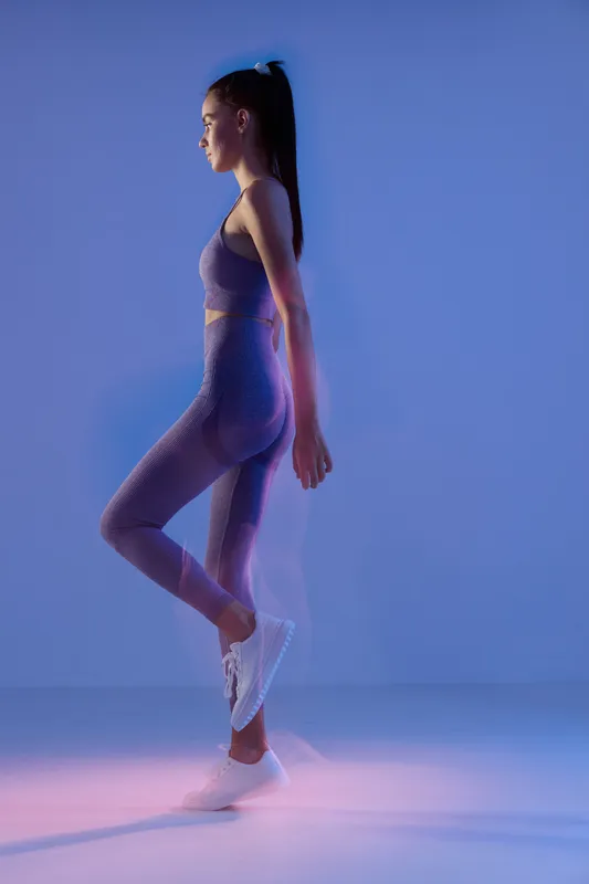 woman sport fitness balancing on one leg in workout outfit with focused expression and blue studio lighting for active lifestyle motivation